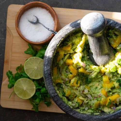stone dish of mango guacamole with fresh cilantro and lime with a dish of salt next to it