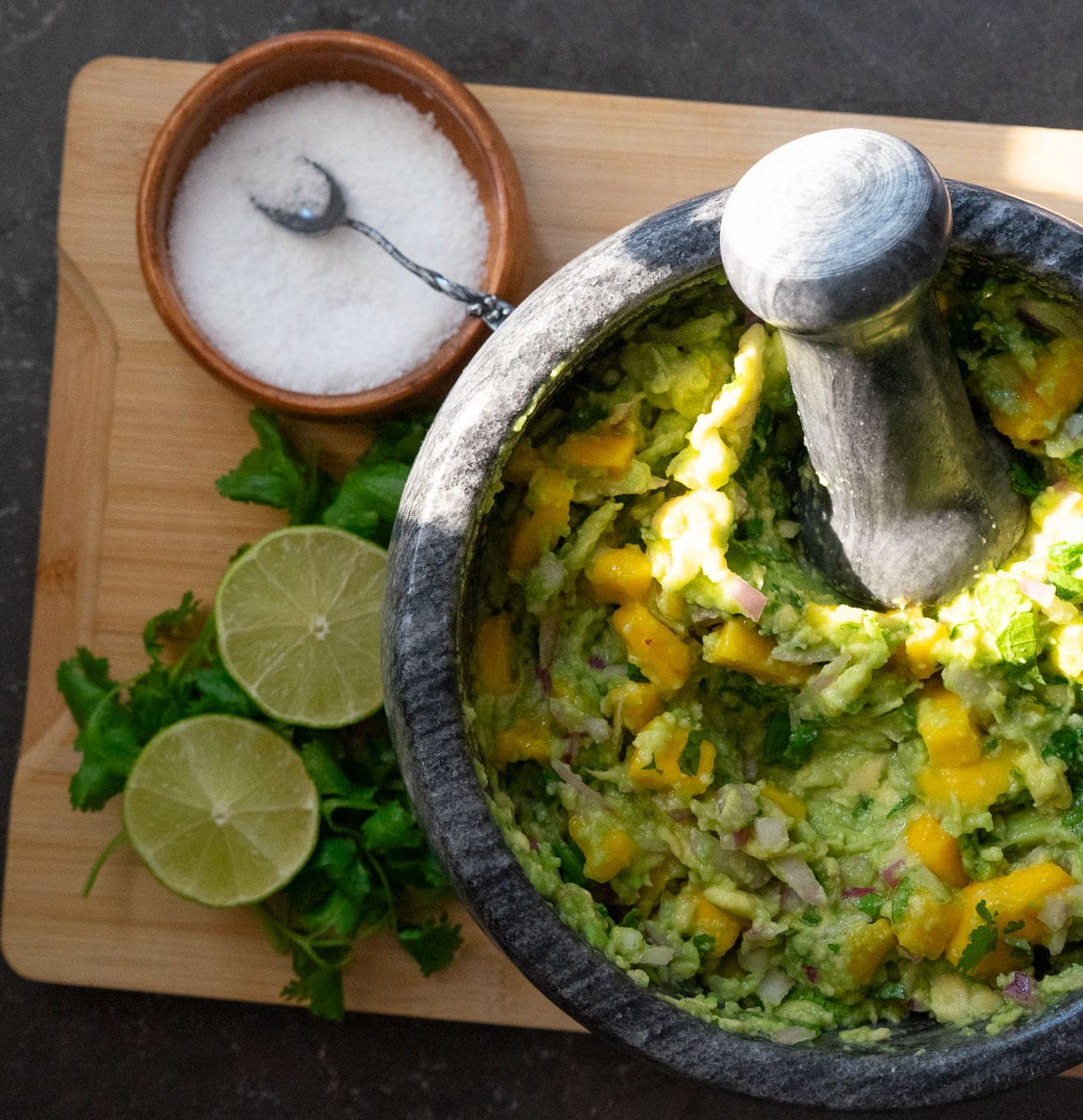 stone dish of mango guacamole with fresh cilantro and lime with a dish of salt next to it