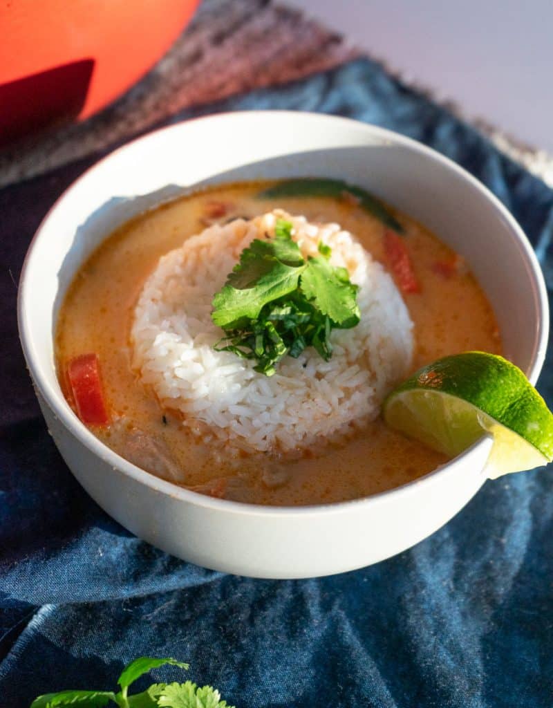 coconut curry soup with rice in the middle of the bowl and a wedge of lim on rim of bowl
