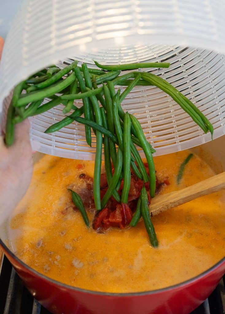adding cut and washed green beans to the pot of soup