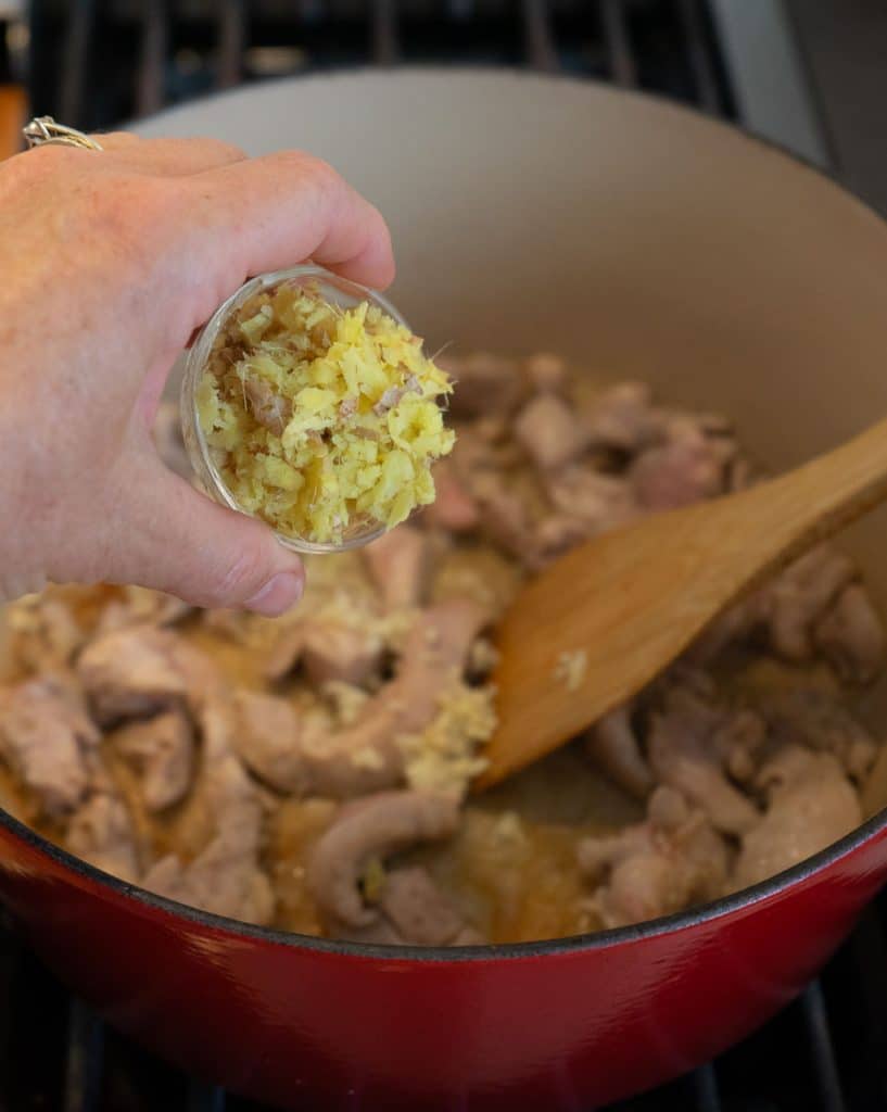 adding ginger and garlic to cooking chicken in dutch oven on stove