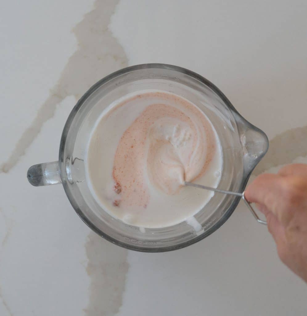 mixing coconut milk and red curry past together in a pourable bowl
