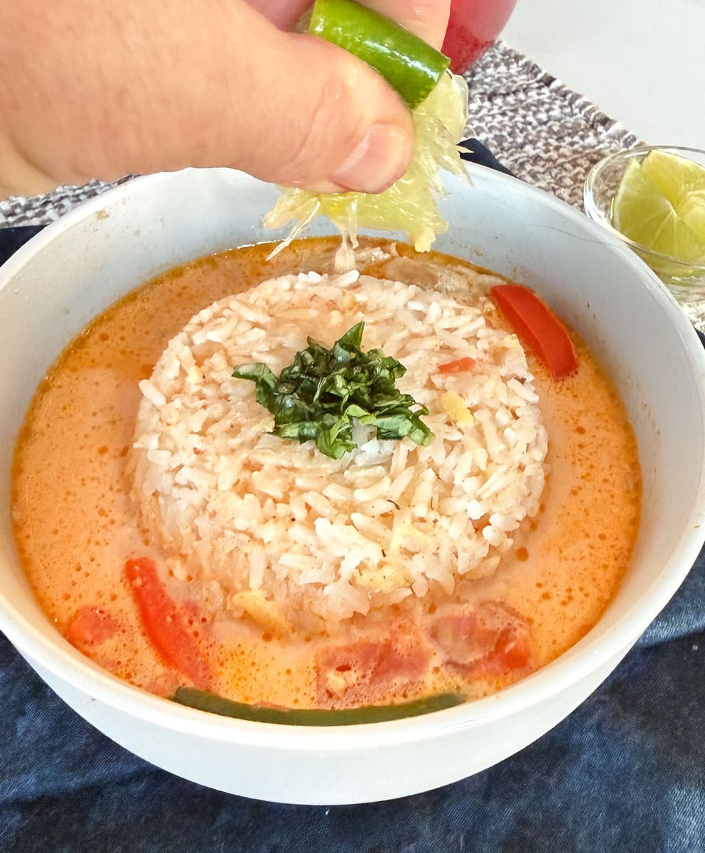 squeezing a lime over coconut curry soup with rice in the middle of the bowl