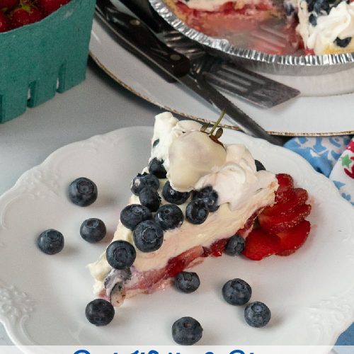 slice of rwb pie on a white plate with a fork on the plate the whole pie is in the back ground with a quart of fresh strawberries on a grey table
