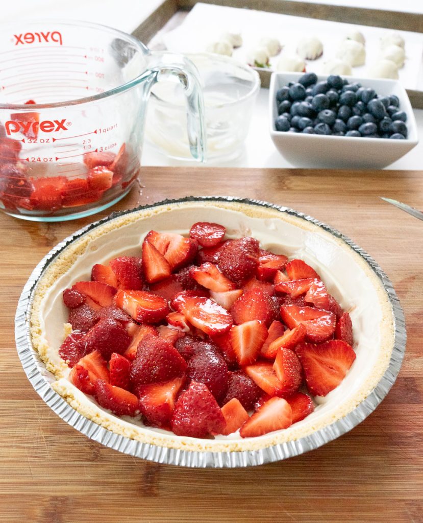 sliced fresh strawberries in the bottom of the white chocolate lined pie crust on a wood cutting board with cups of berries in the back ground