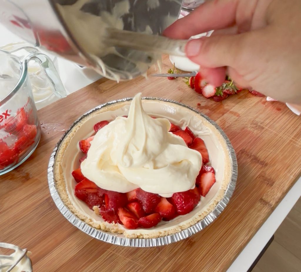 scooping cheesecake filling over the strawberries in the pie crust