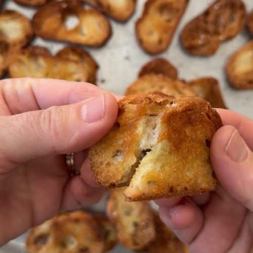 hands breaking a crostini in half over a pan of crostinis