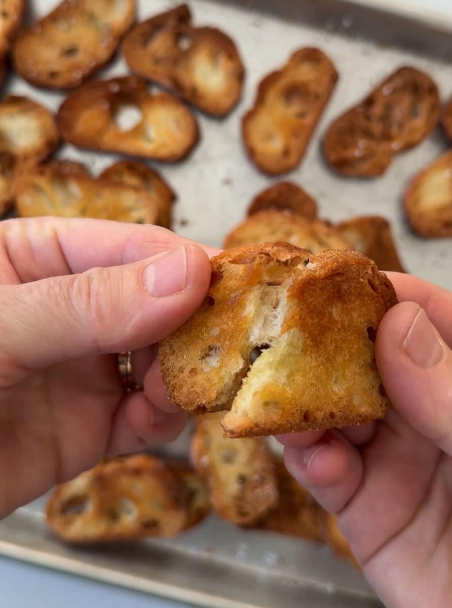 hands breaking a crostini in half over a pan of crostinis