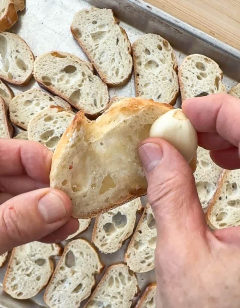 rubbing a slice of baguette with clove of garlic