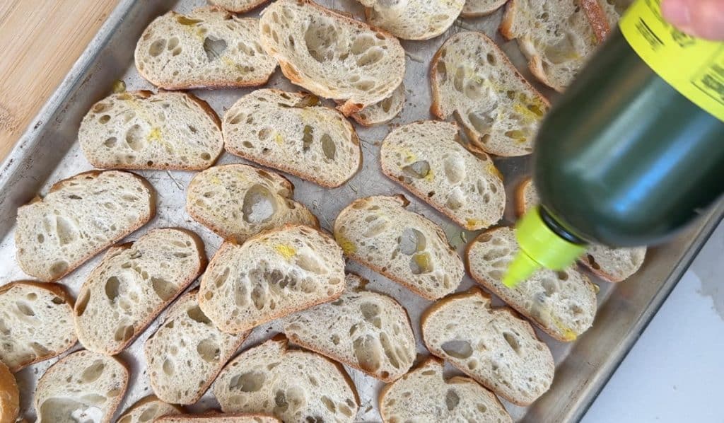 drizzling olive oil over each crostini on a baking sheet