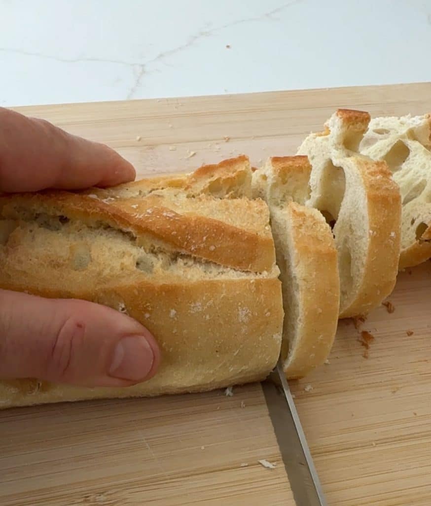 slicing a baguette on a wood cutting board