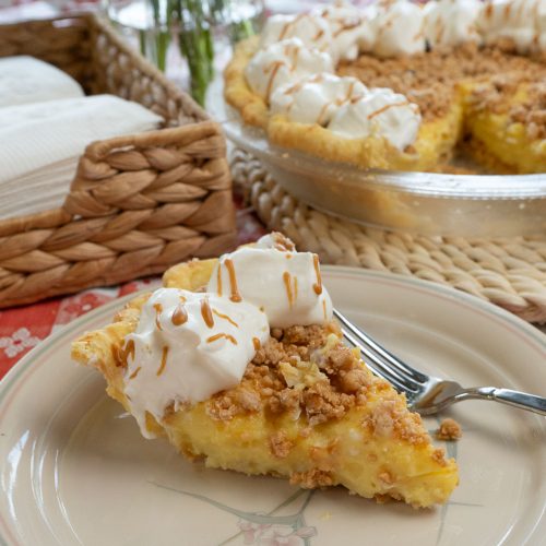 slice of peanut butter pie on a plate with a fork on the plate whole pie with a piece taken out is in the back ground