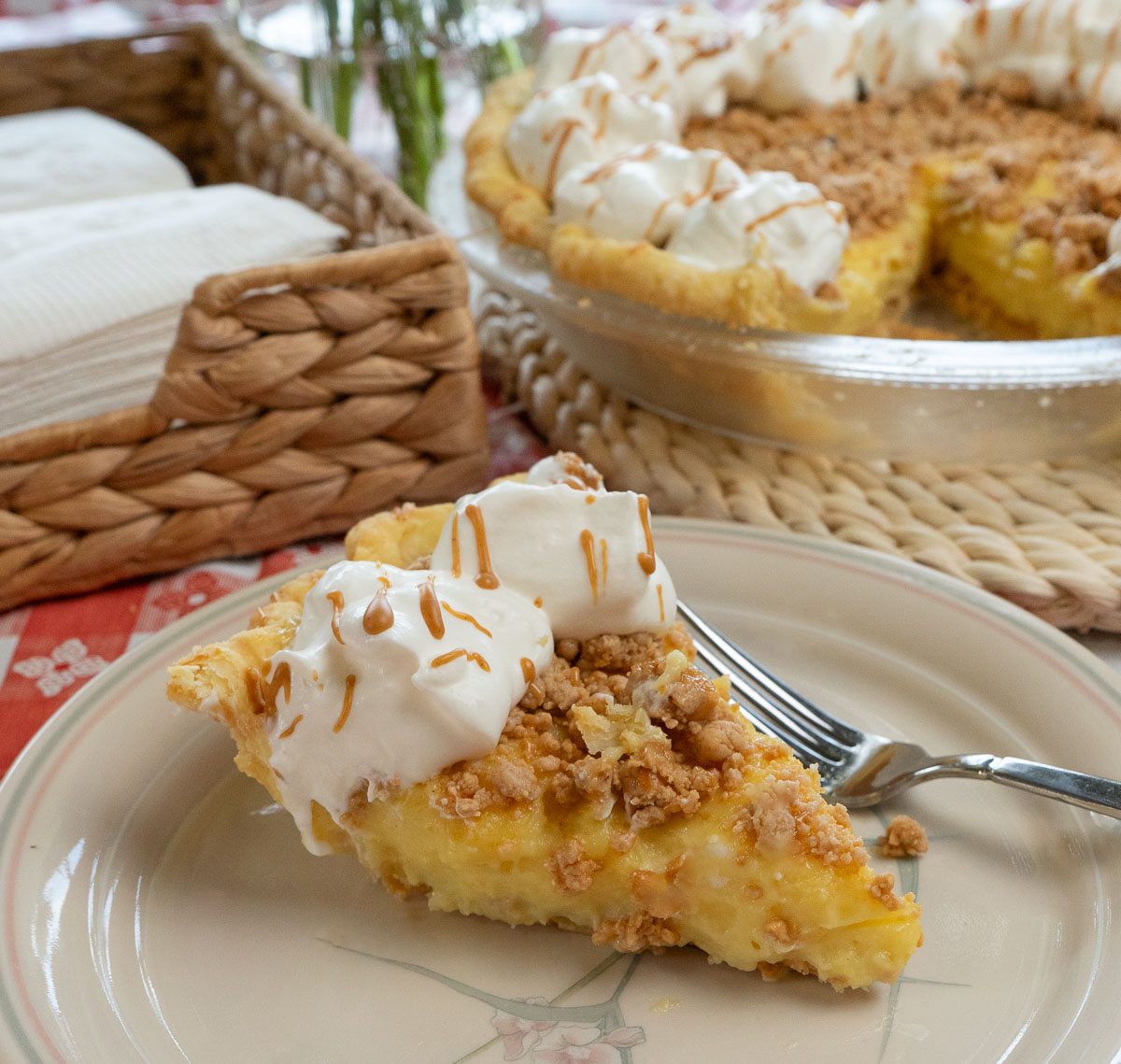 slice of peanut butter pie on a plate with a fork on the plate whole pie with a piece taken out is in the back ground