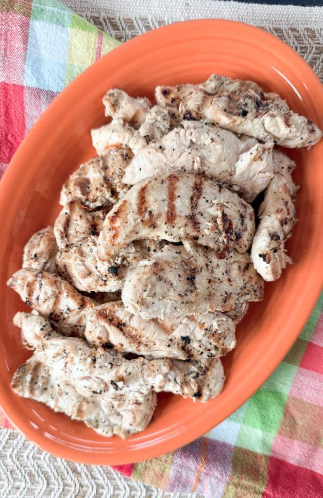 grilled lemon pepper chicken tenderloins on an orange platter that is on a colorful kitchen towel
