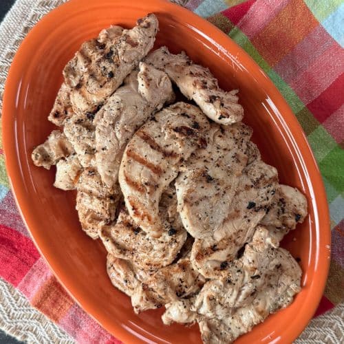 grilled lemon pepper chicken tenderloins on an orange platter that is on a colorful kitchen towel