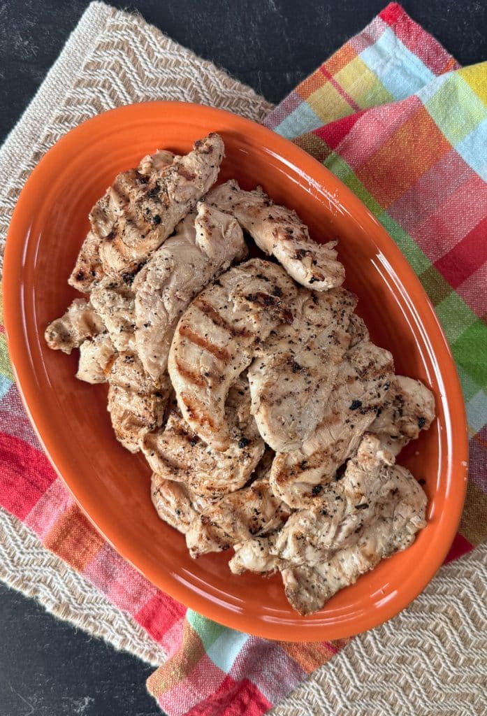 grilled lemon pepper chicken tenderloins on an orange platter that is on a colorful kitchen towel