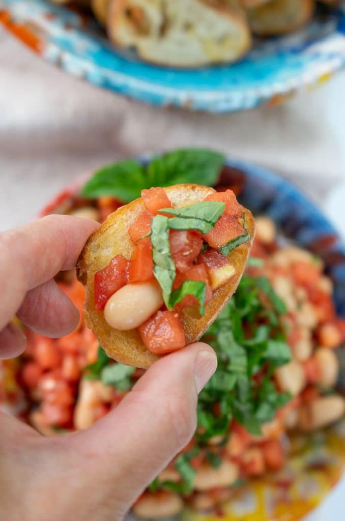 fingers holding a bread toast with bruschetta on top 