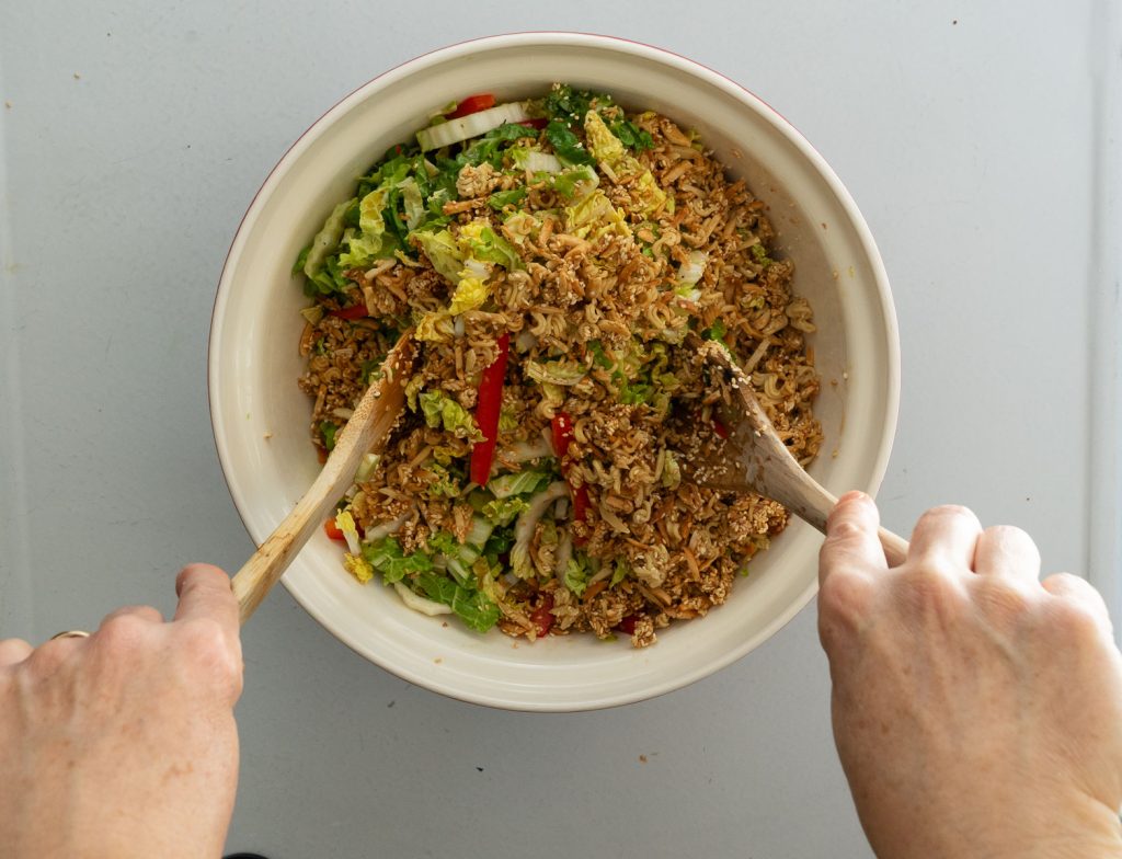 asian slaw with toasted ramen, hands tossing salad