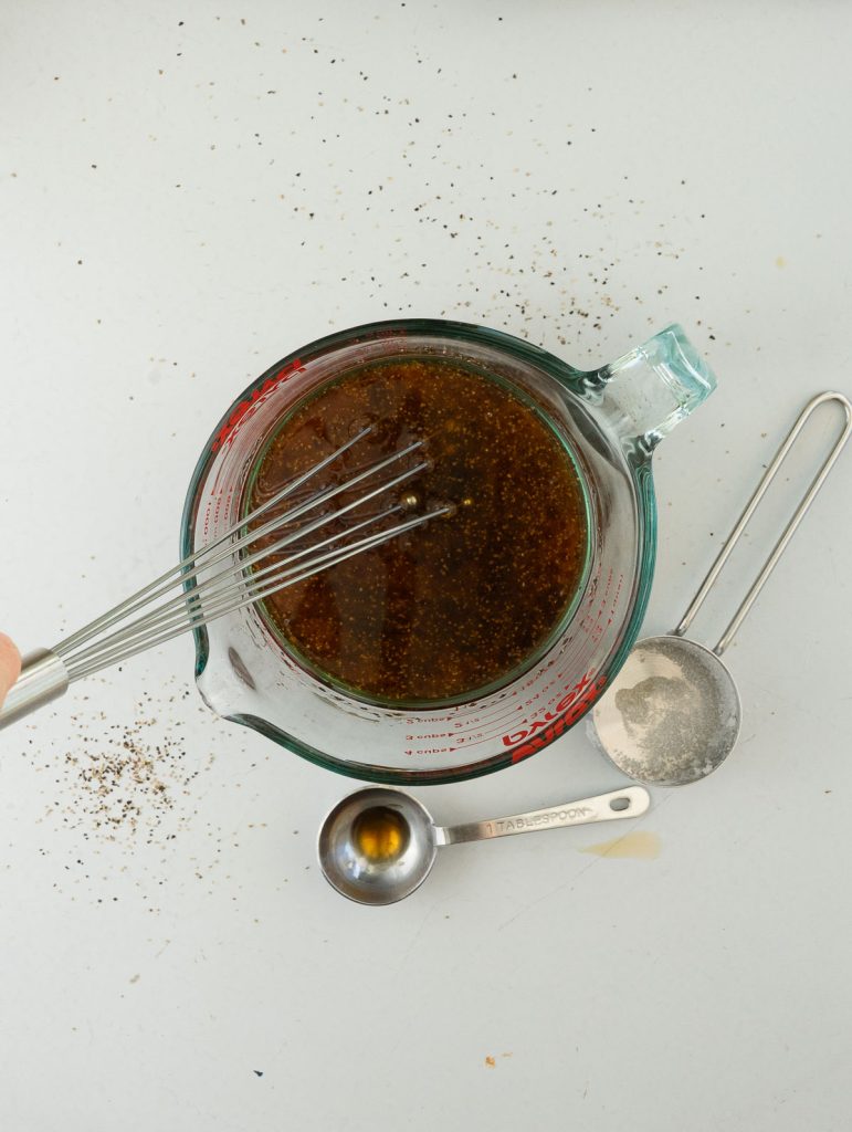 whisk in a glass measuring cup with salad dressing ingredients on a white back ground