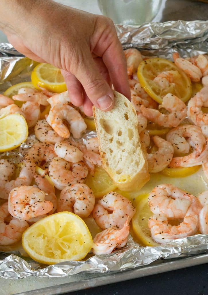 hand dipping bread into the lemon butter on the tray of grilled shrimp and lemons