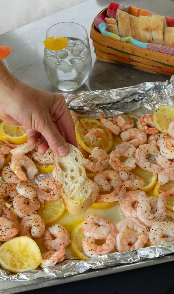 hand dipping bread into the lemon butter on the tray of grilled shrimp and lemons 