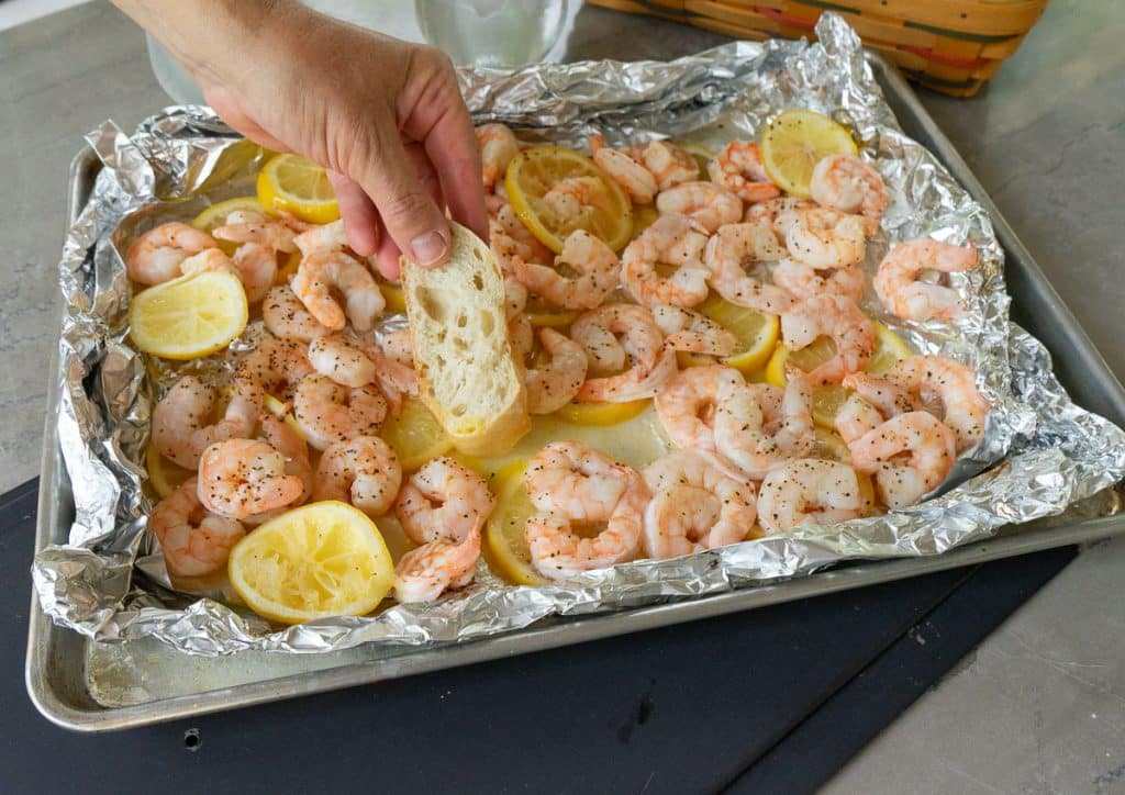 dipping bread in the lemon butter beach shrimp are on a baking sheet 