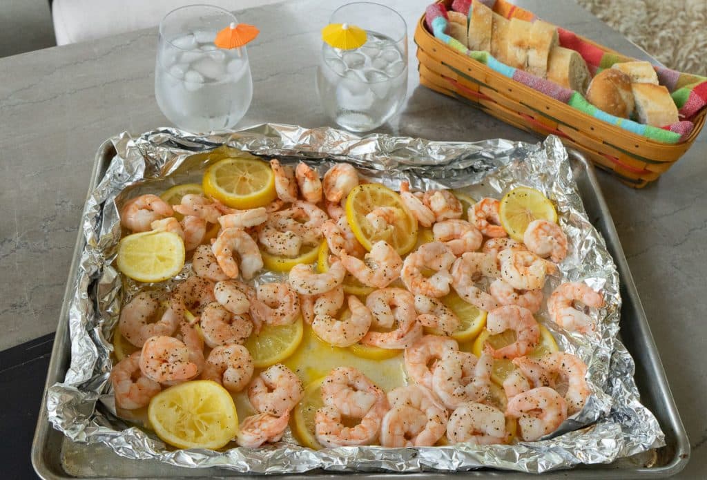 cooked shrimp with lemon on a table outside with a basket of sliced bread and drinks