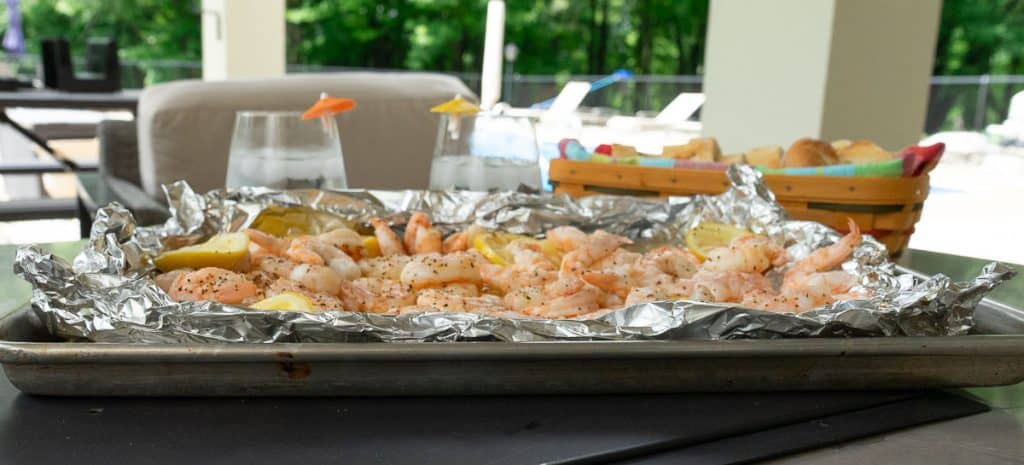 beach shrimp on table outside with a basket of bread and drinks in the back ground