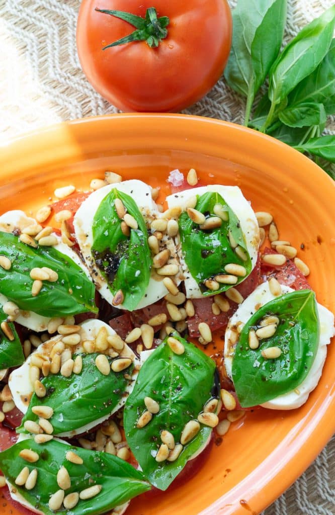 caprese salad on an orange platter with some fresh basil and a whole tomato in the top of the photo