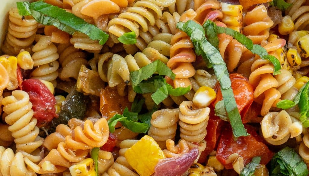 close of pasta salad showing noodles and vegetables and fresh basil