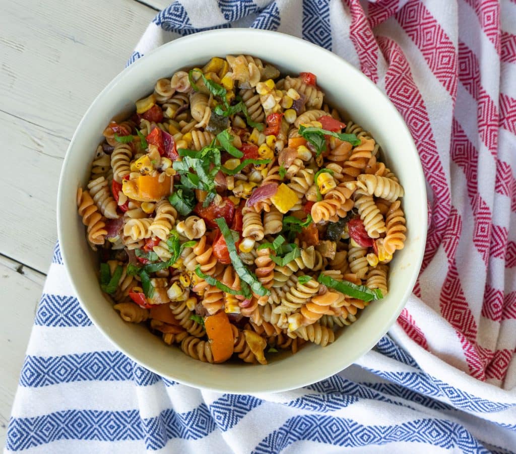 bowl of pasta salad on a white picnic table with a red white and blue cloth under the bowl