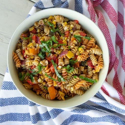 bowl of pasta salad on a white picnic table with a red white and blue cloth under the bowl