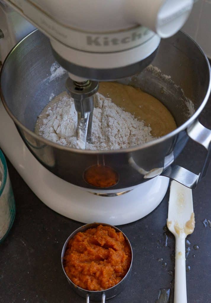 Mixing bowl with pumpkin bundt batter, a measuring cup of pumpkin next to the stand mixer