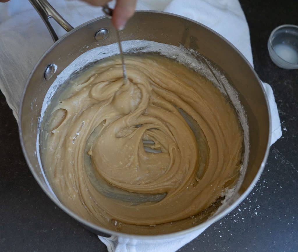 whisking caramel frosting in a saucepan that is sitting on a white tea towel on a black countertop
