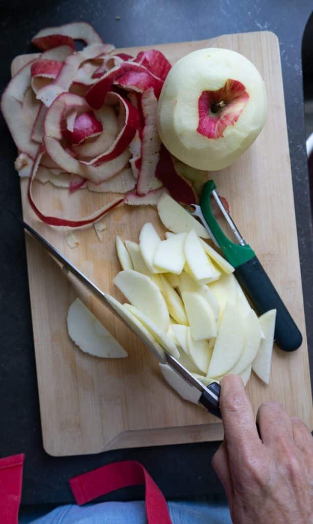 apples on a cutting board in various stages of being peeled and sliced. 