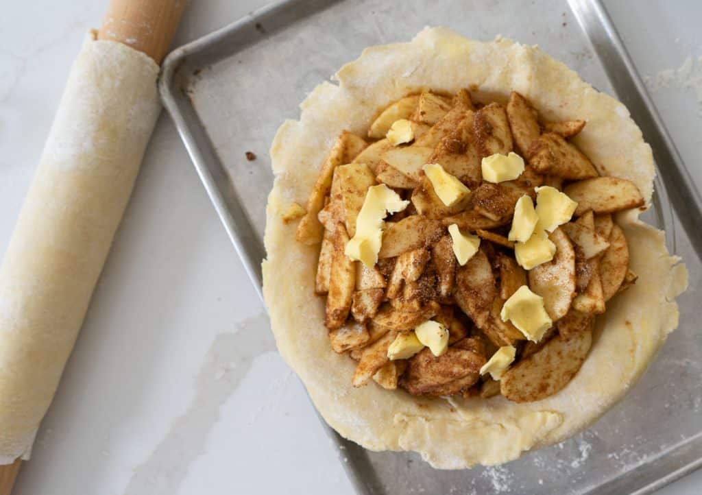 apples in bottom pie crust with the second pie crust wrapped around the rolling pin sitting beside the pie plate