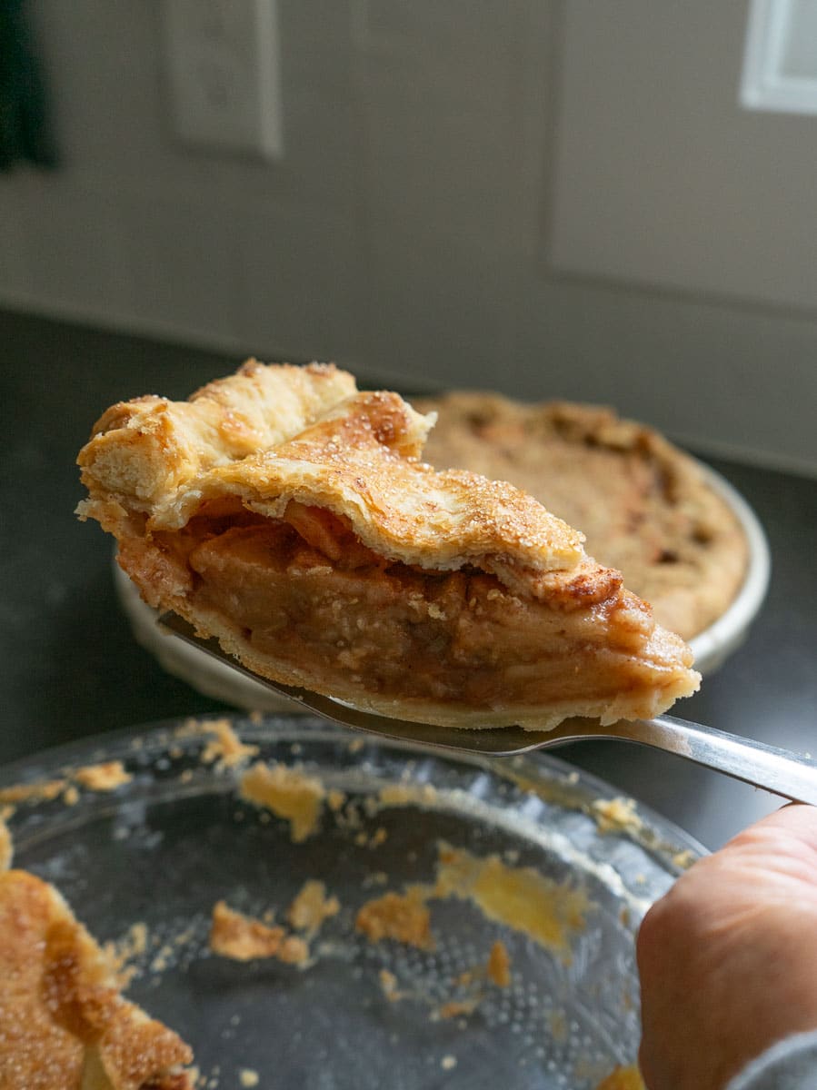 slice of apple pie on a spatula being held over pie plate