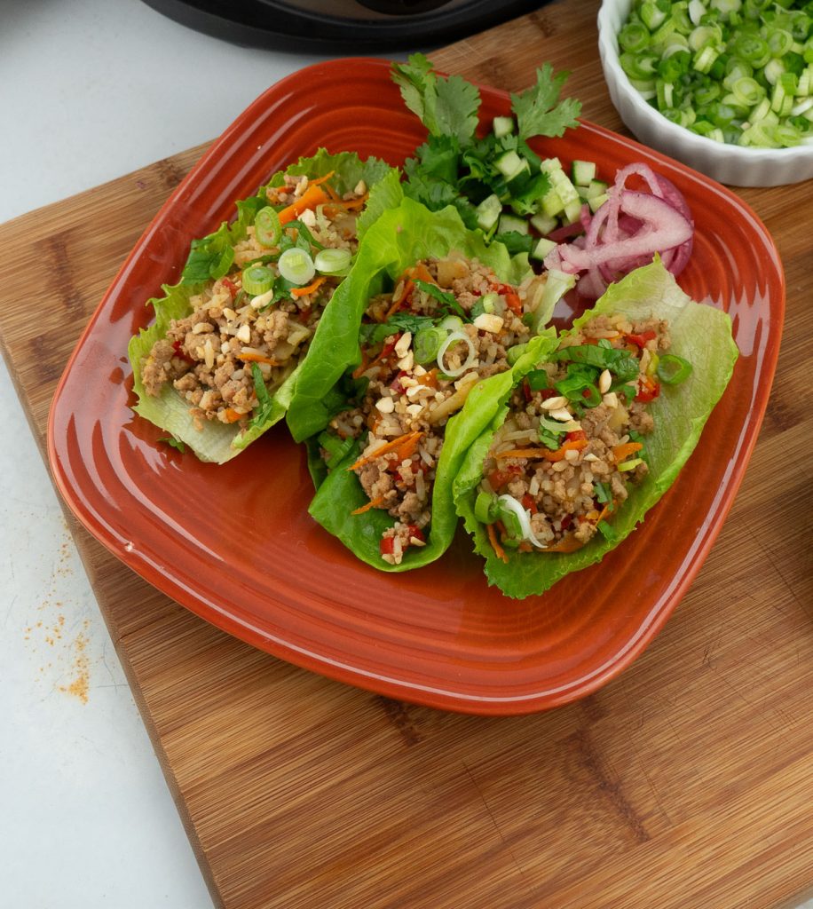 slow cooker chicken lettuce wraps on a brown plate on a wood cutting board