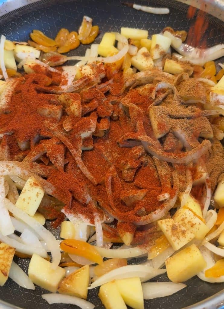 onions, apples, dried apricots, and spices sauteing in a pan on the stove top