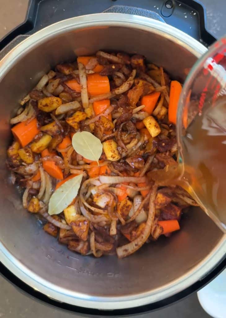 bay leaves added to the slow cooker over onions pouring beef stock into the pot