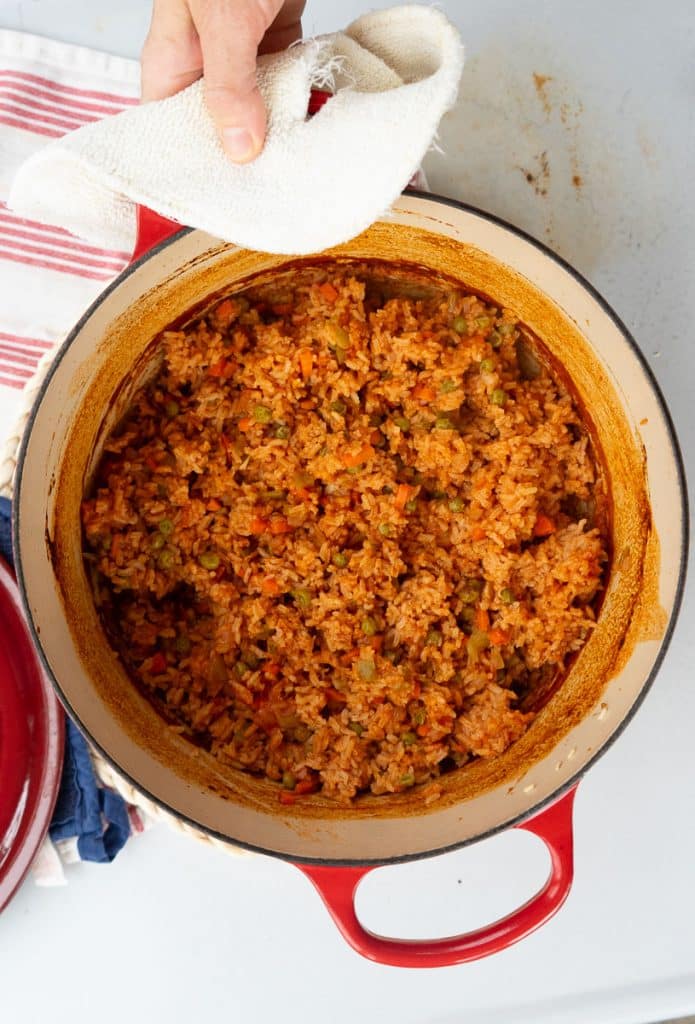 spanish rice in a red dutch oven after being taken out of the oven and having fluffed the rice, a hand is holding the top of the pot with a potholder