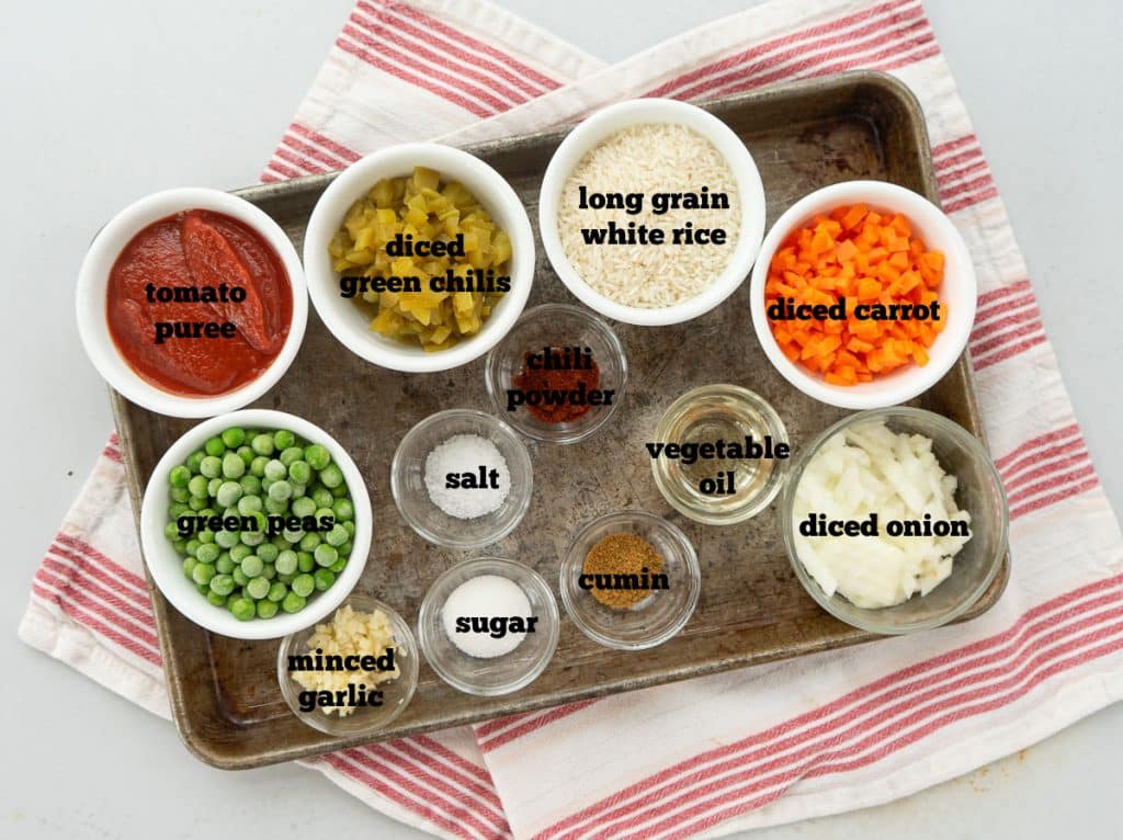 ingredients for easy authentic spanish rice laid out on a baking sheet on a table with a striped napkin underneath