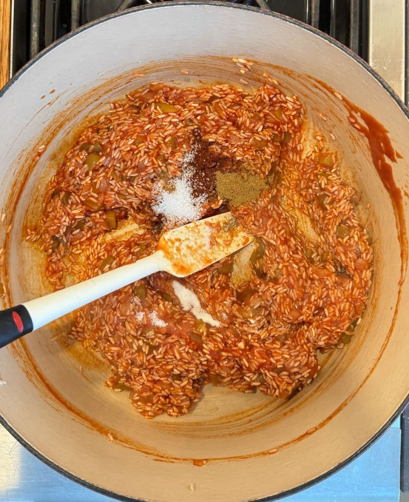 adding spices to the spanish rice a spatula is stirring the rice