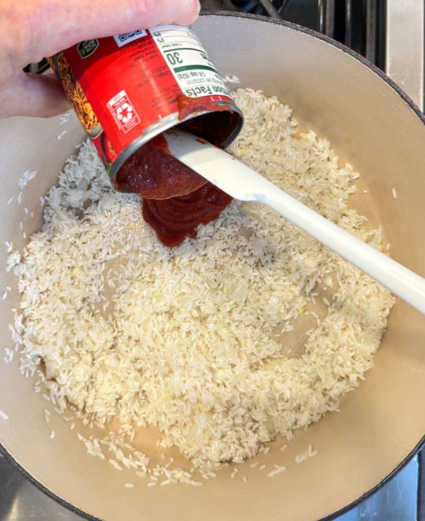 adding the tomato puree to the toasted rice in the pot on top of the stovetop hand scooping puree out of can over rice