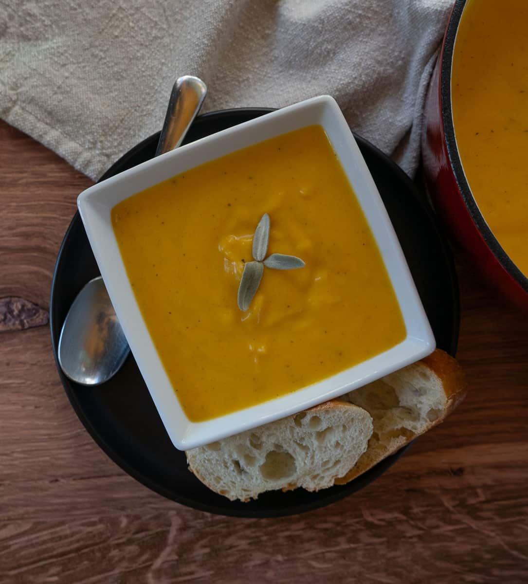 roasted butternut squash soup in a white square bowl with bread on the side