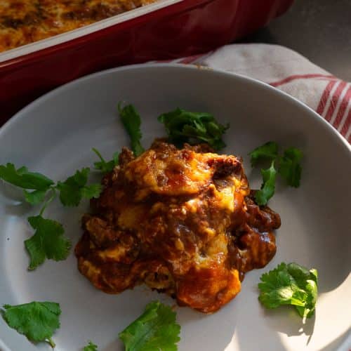 plated beef and bean enchiladas with the whole pan of casserole behind the plate on a kitchen countertop
