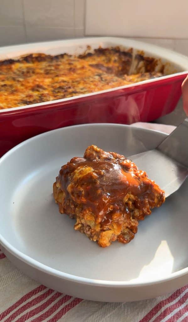 scooping layered beef and bean casserole on to a gray plate with a large spatula
