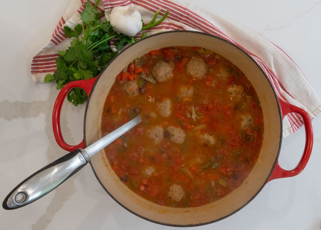 large red pot sitting on a white countertop with a red striped towel tucked around it with cilantro and a bulb of garlic off the the top left corner