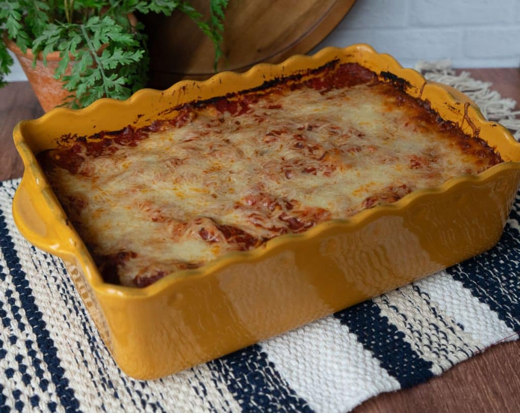 full dish of spaghetti pie sitting on a wood counter with a white tile back splash, dish is also sitting on a blue, white, and tan striped place mat