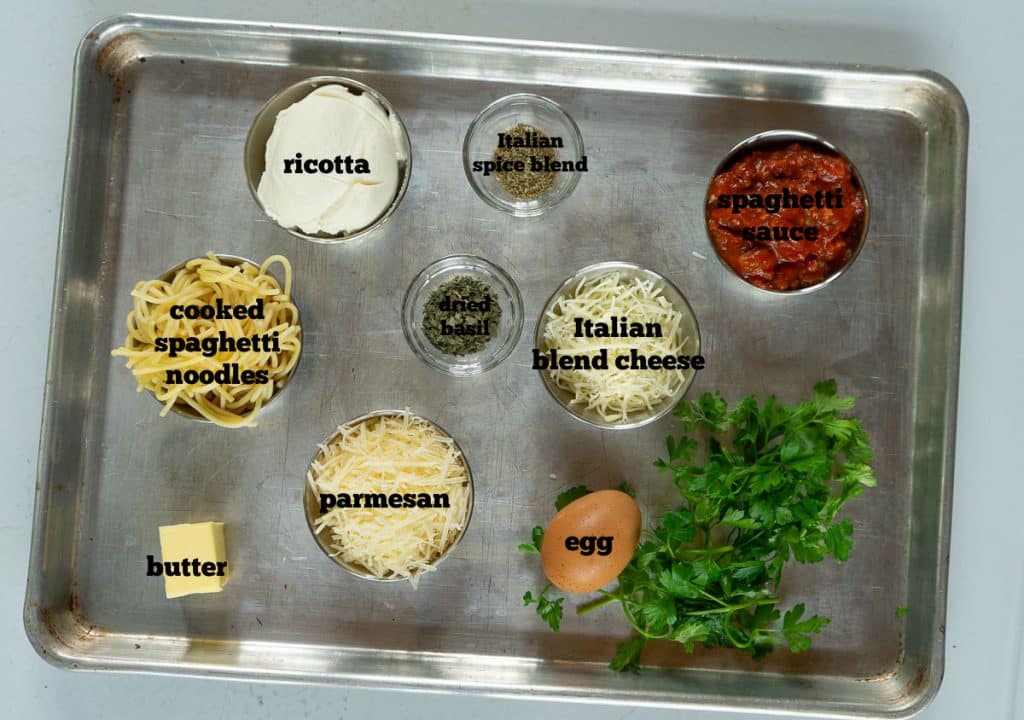 ingredients for spaghetti pie on a baking sheet that is sitting on a gray countertop